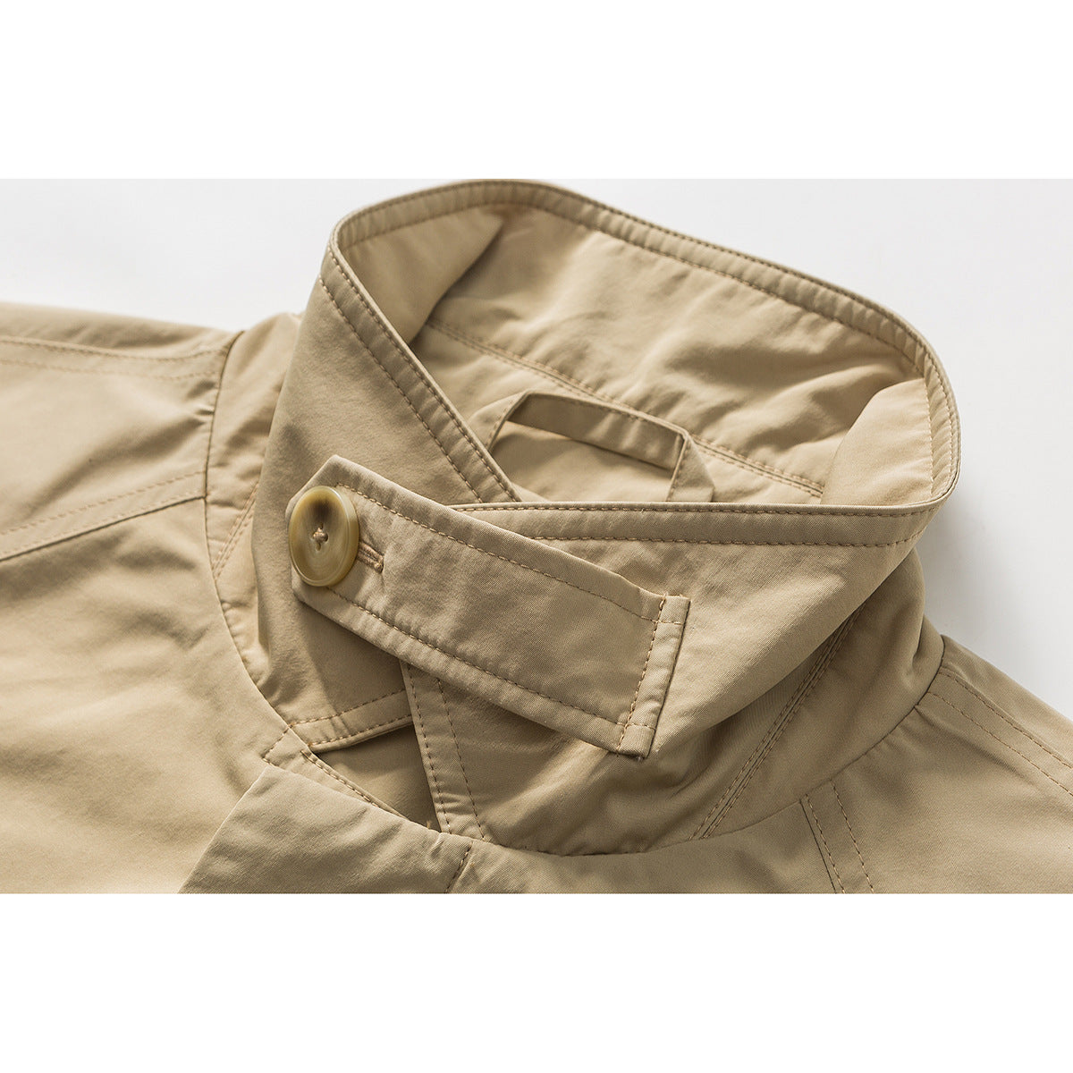 Close-up of a tan coat’s high collar and buttoned throat latch with visible stitching.