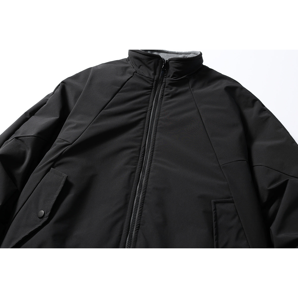 Close-up of a black zip-front jacket with a stand collar, angled seams, and snap-button pocket flaps.