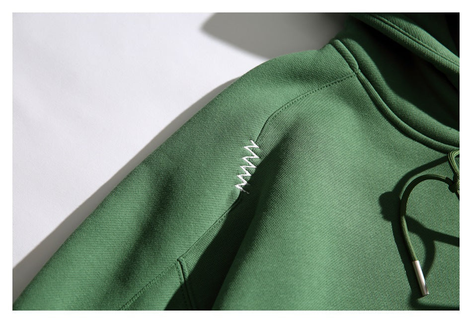 Close-up of a small white zigzag embroidery detail on the green hoodie’s shoulder.