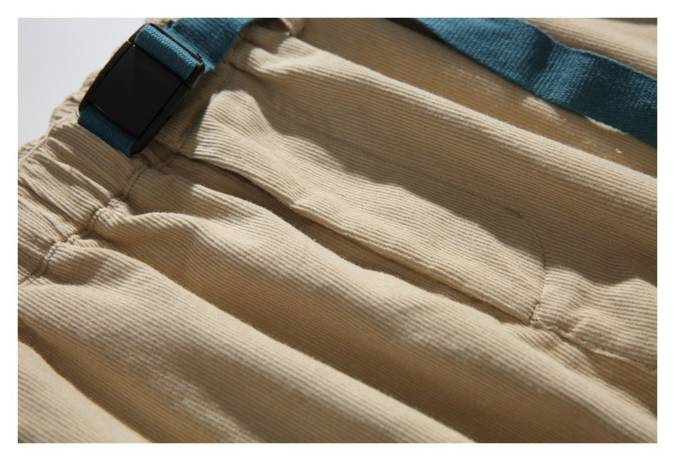 Close-up of tan ribbed trousers with a teal webbing belt and black buckle.