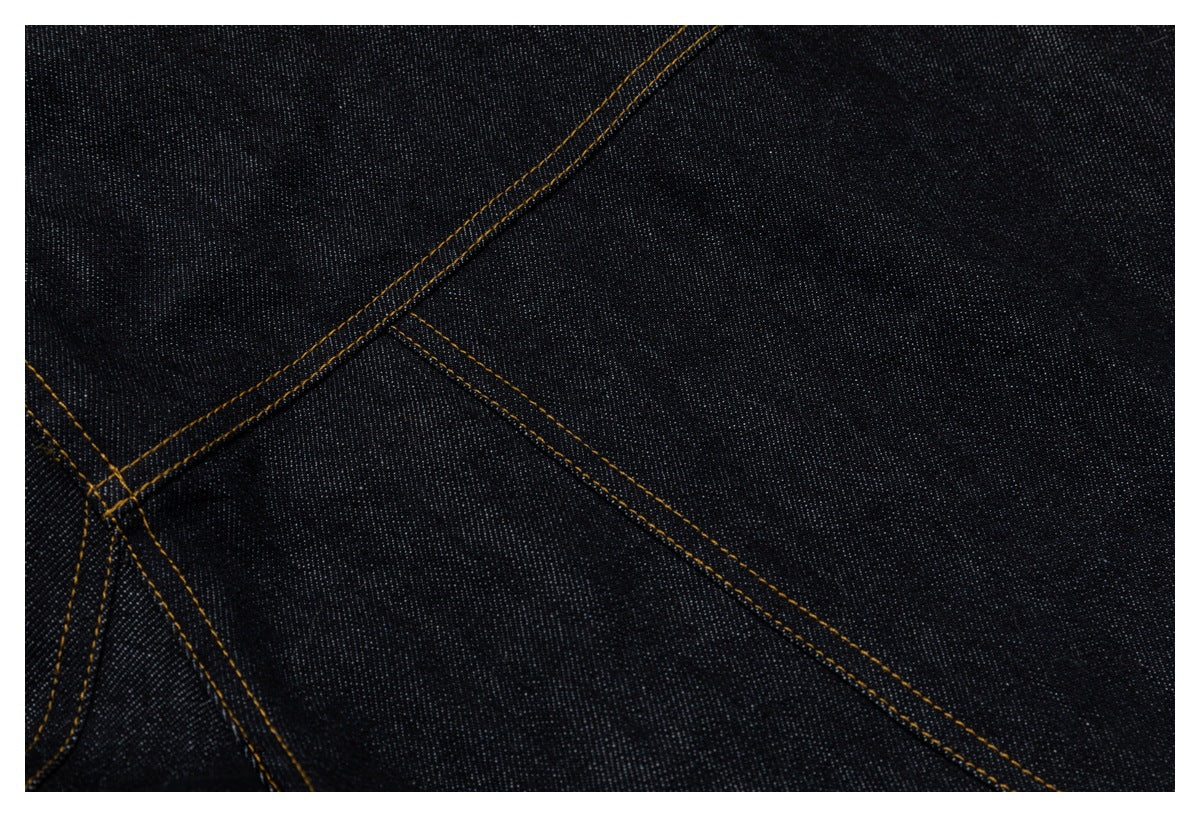 Close-up of dark indigo denim panels and intersecting tan double-stitching.