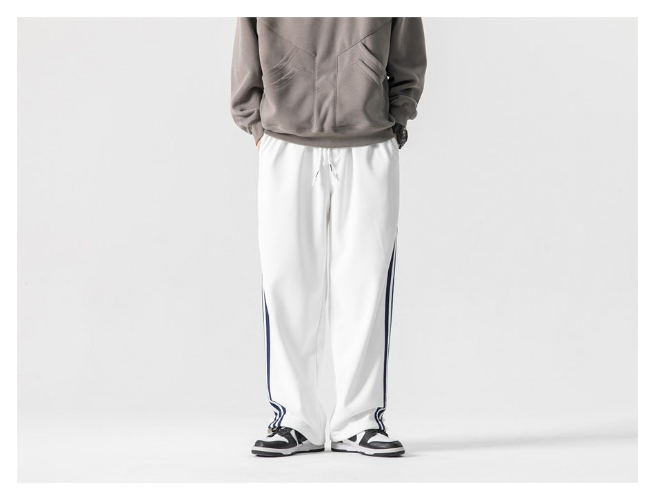 Model wearing white wide-leg pants with navy side stripes, gray sweatshirt and sneakers, cropped front view