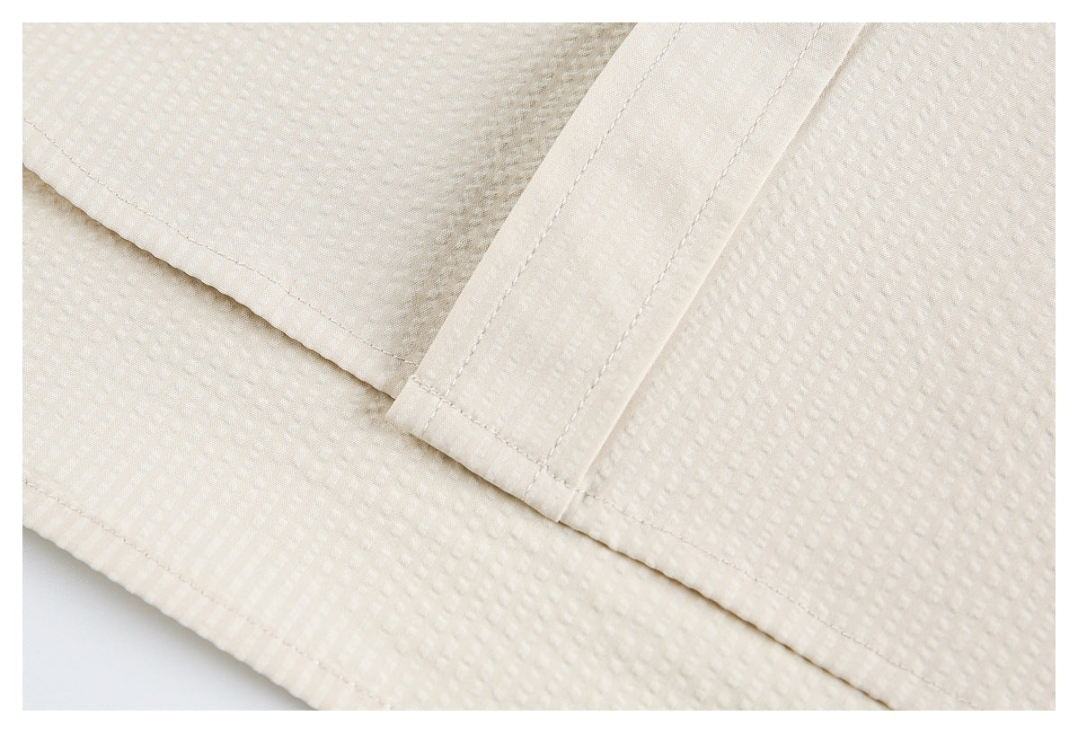 Close-up of the off-white garment's stitched hem and overlapping placket edge.