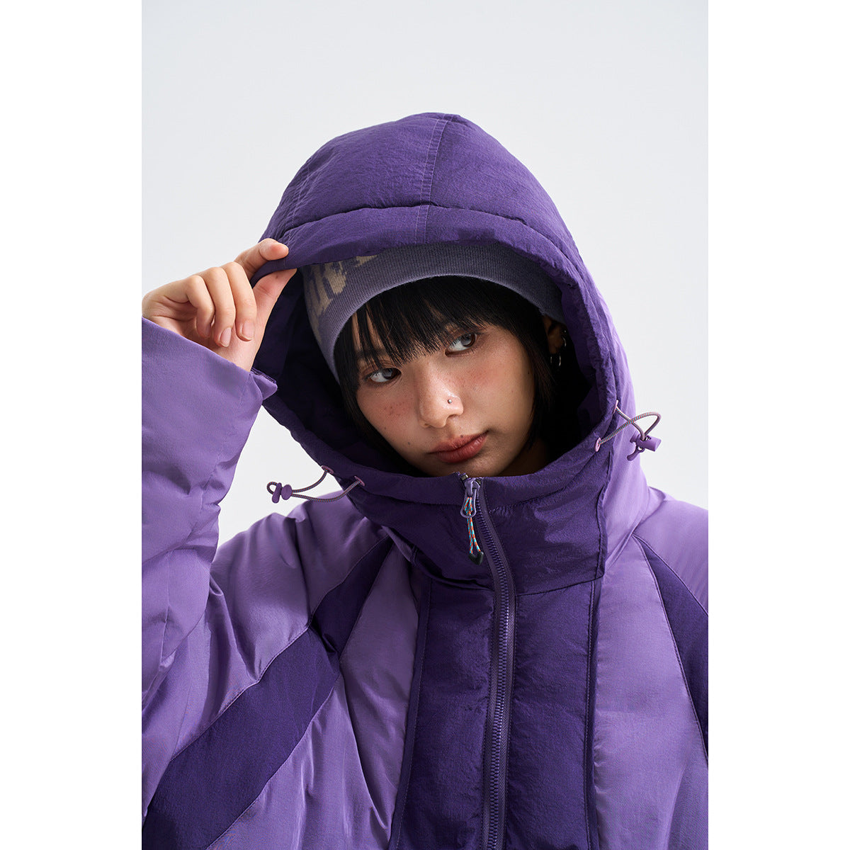 Close-up of a model in a purple hooded jacket, showing the adjustable hood, colorful drawcords, and front zipper.