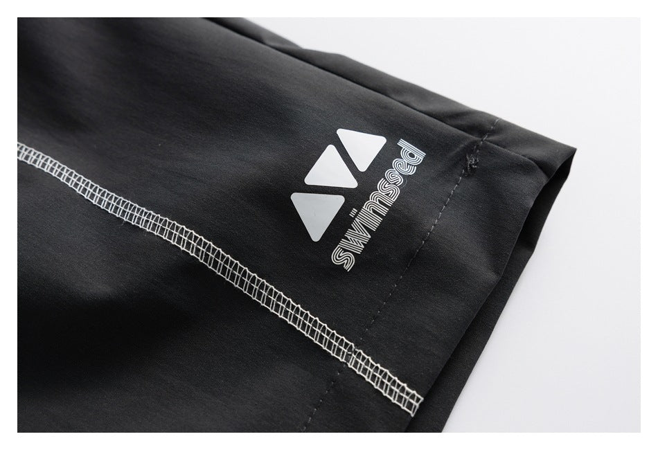Close-up of a black pants hem with a white emblem and lettering above a line of contrasting overlock stitching.