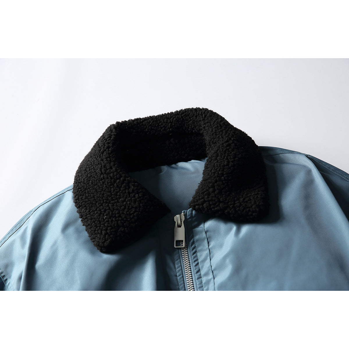 Close-up of a light blue jacket with a black textured collar and silver front zipper.