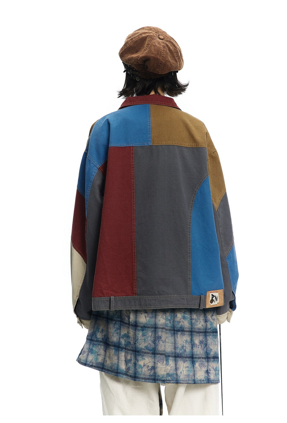 Back view of a model wearing a patchwork jacket with large blue, charcoal, burgundy, and tan panels.