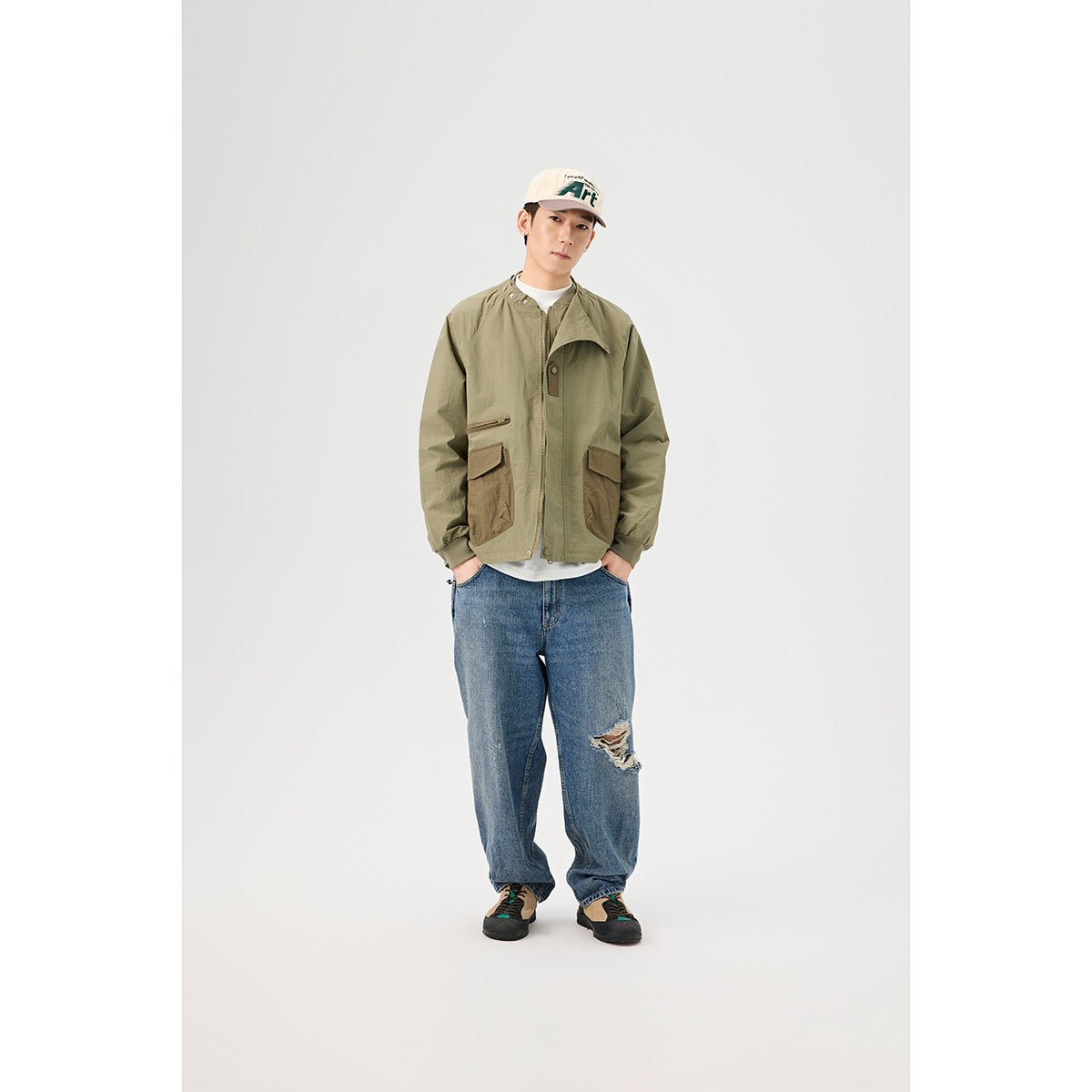 Model wearing an olive utility jacket partly open, with brown pockets and blue jeans, shown from the front.