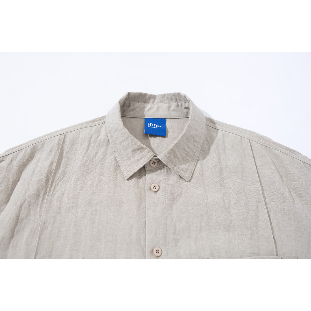 Close-up of a light beige short-sleeve shirt collar, buttons, and blue neck label.