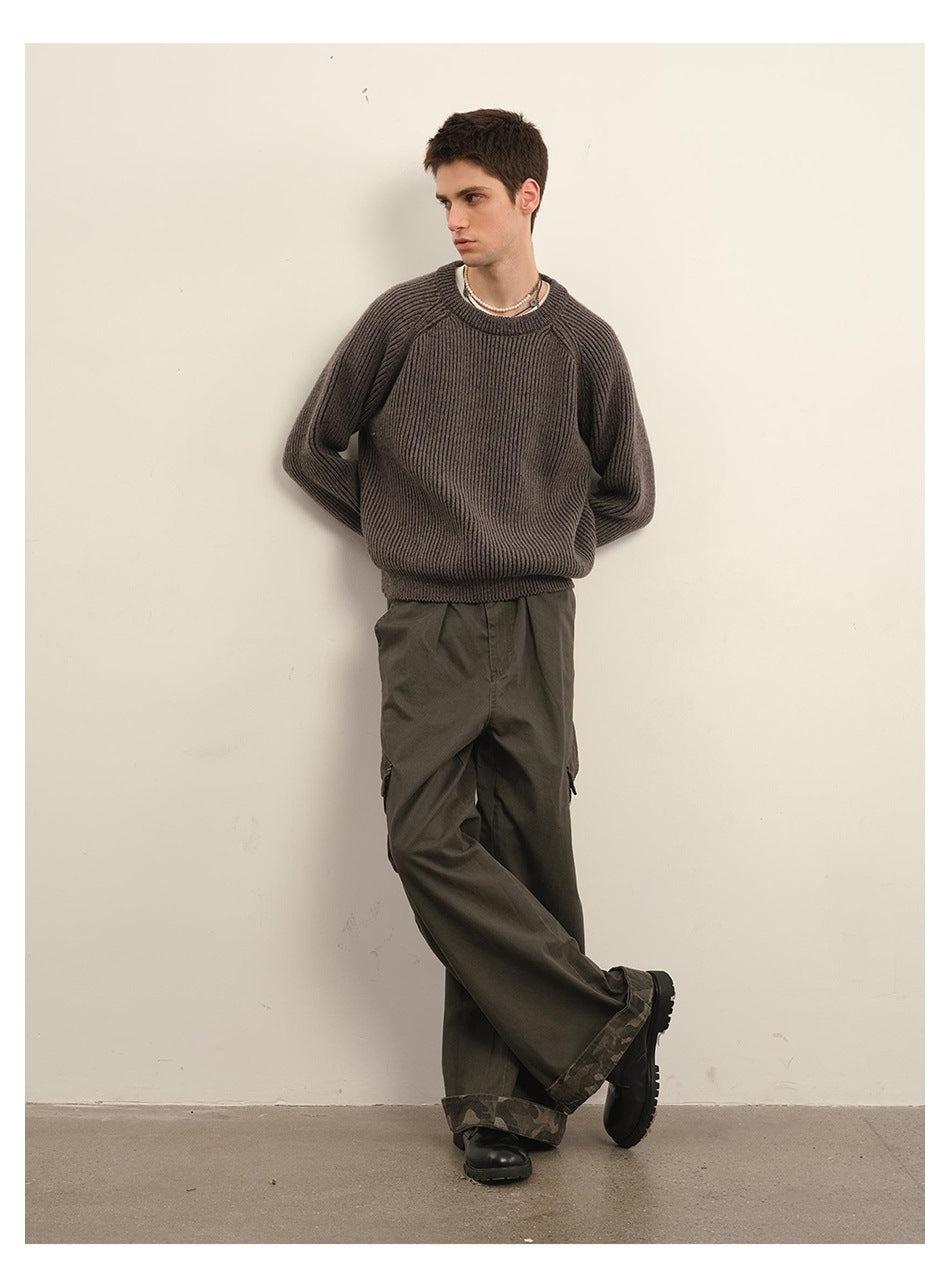 Model leaning on a wall wearing a dark gray rib-knit crewneck sweater with olive cargo pants