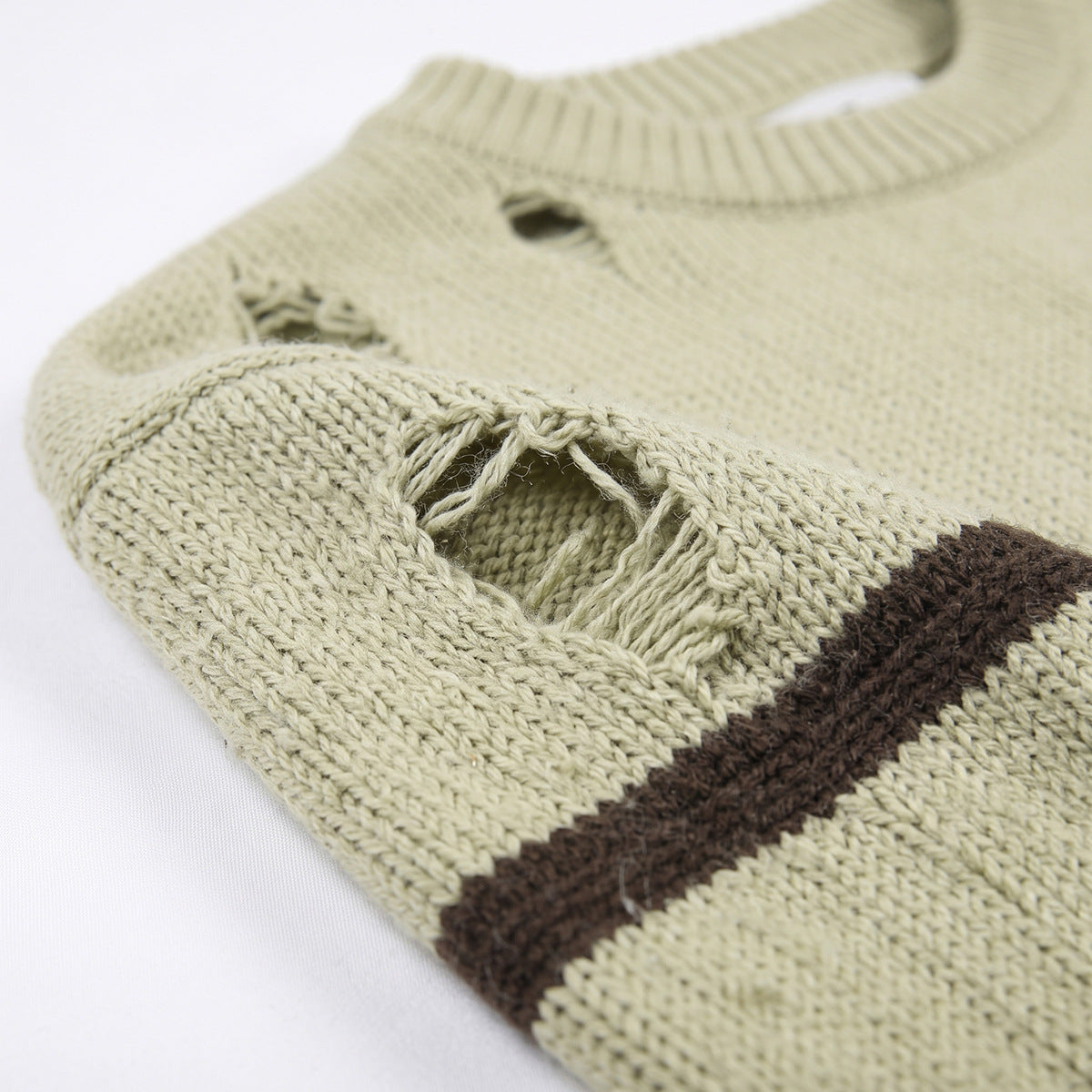 Close-up of a pale beige knit sweater with a ribbed crew neck, brown stripe, and distressed holes.