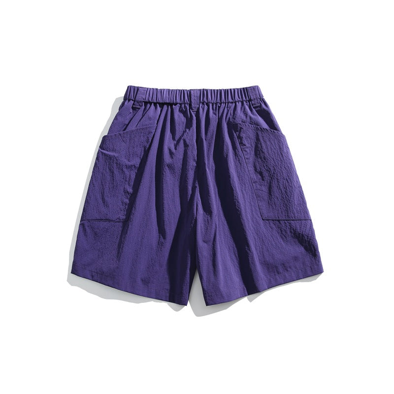 Purple shorts with an elastic waistband and large patch pockets on both sides, shown against white.