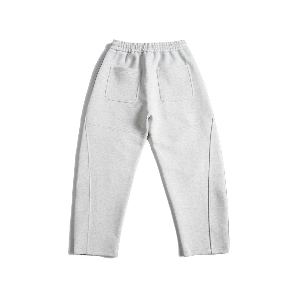 Back view of light gray jogger pants with an elastic waistband, two patch pockets, and stitched leg panels.