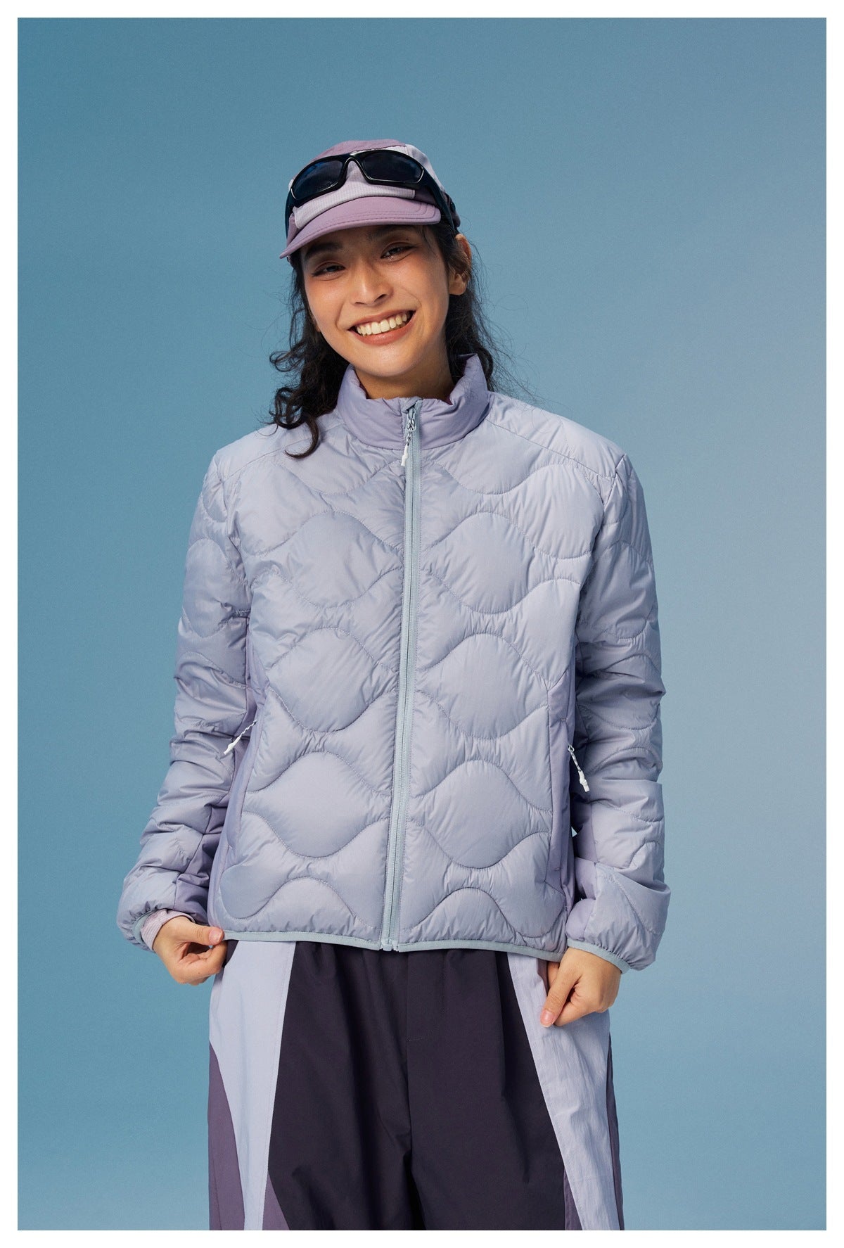 Front view of a model wearing a pale lavender wave-quilted zip jacket with a stand collar and side pockets.