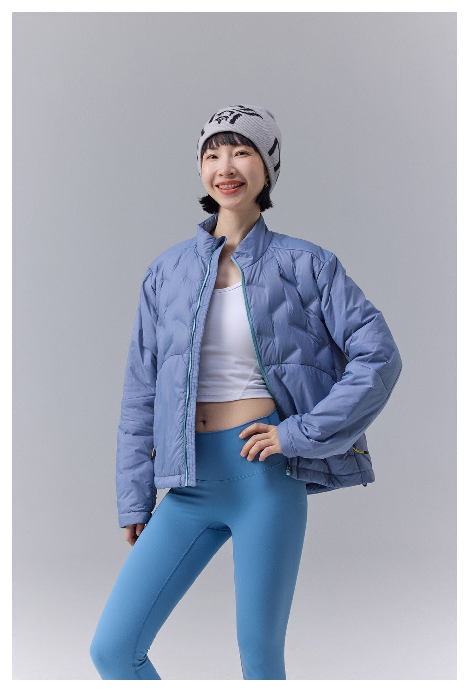 Closer front view of a model in a light blue quilted jacket with turquoise zipper trim and zip pockets.