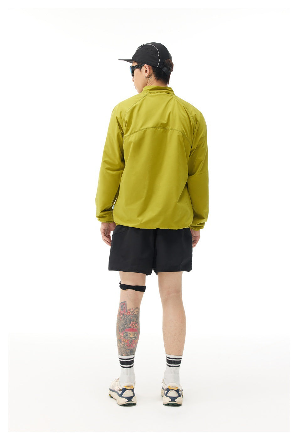 Rear view of a model wearing a chartreuse zip jacket and black shorts.