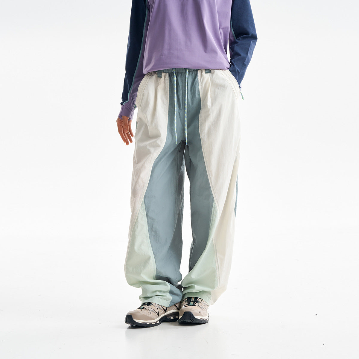 Cropped view of a model wearing loose color-block pants in cream, sage, and blue-gray with a drawstring waist.