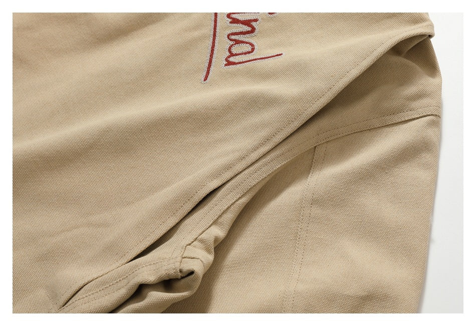 Close-up of a beige garment seam with a folded edge and partial red embroidery.