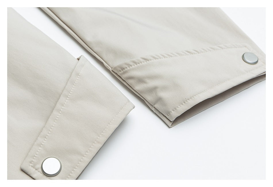 Close-up of light beige garment cuffs with stitched edges and large round metal snaps.