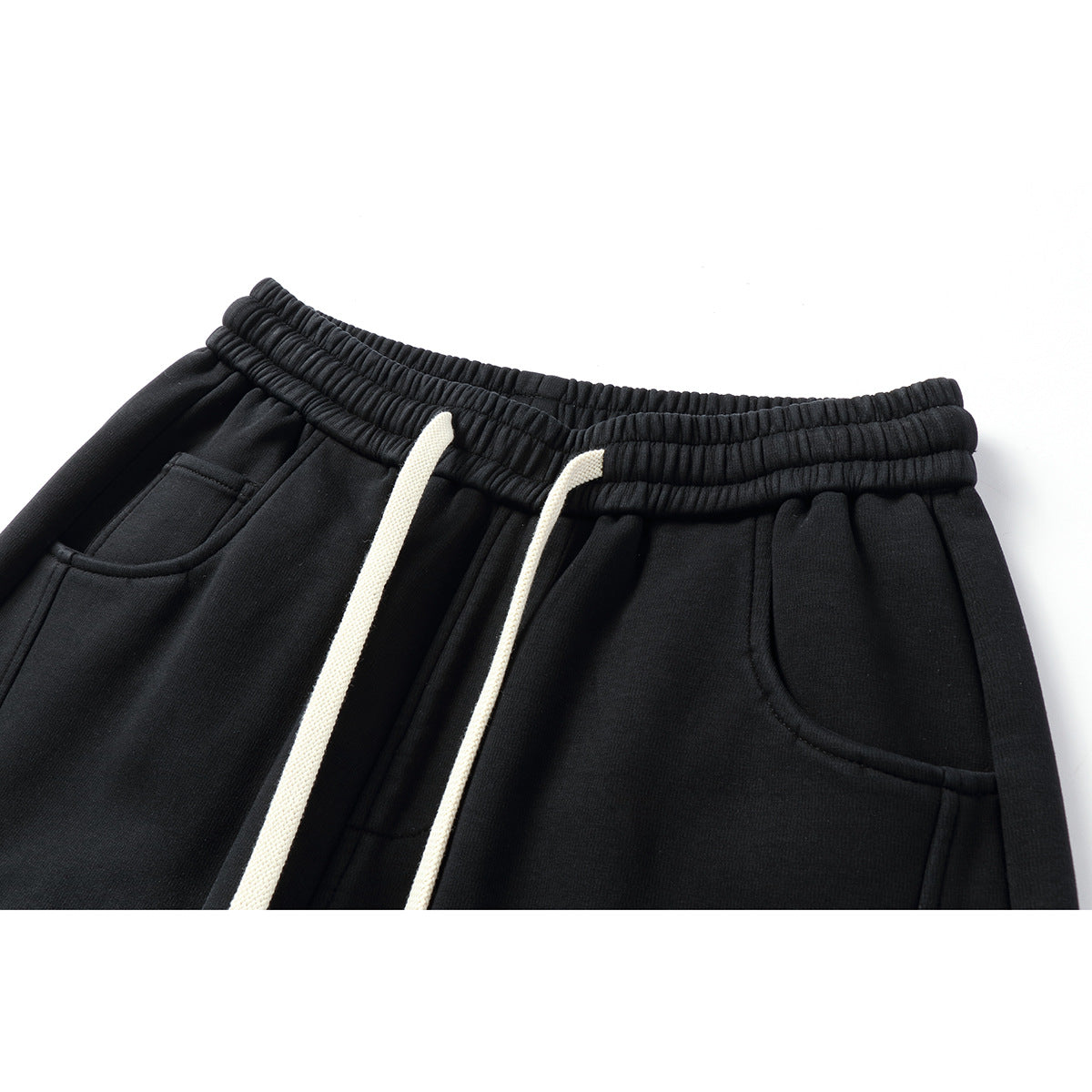 Close-up of black pants with a gathered elastic waistband, cream drawstrings, and curved front pockets.