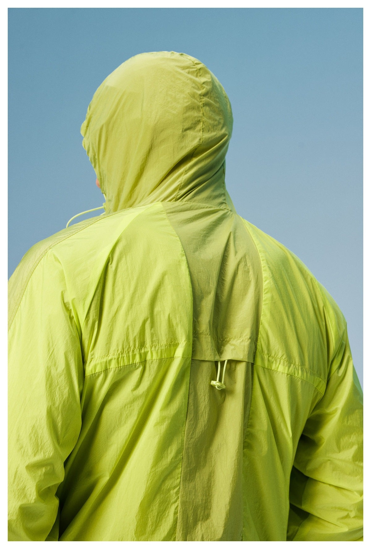 Back view of a model wearing a lime-green hooded jacket with a center back vent and adjustable drawcord.