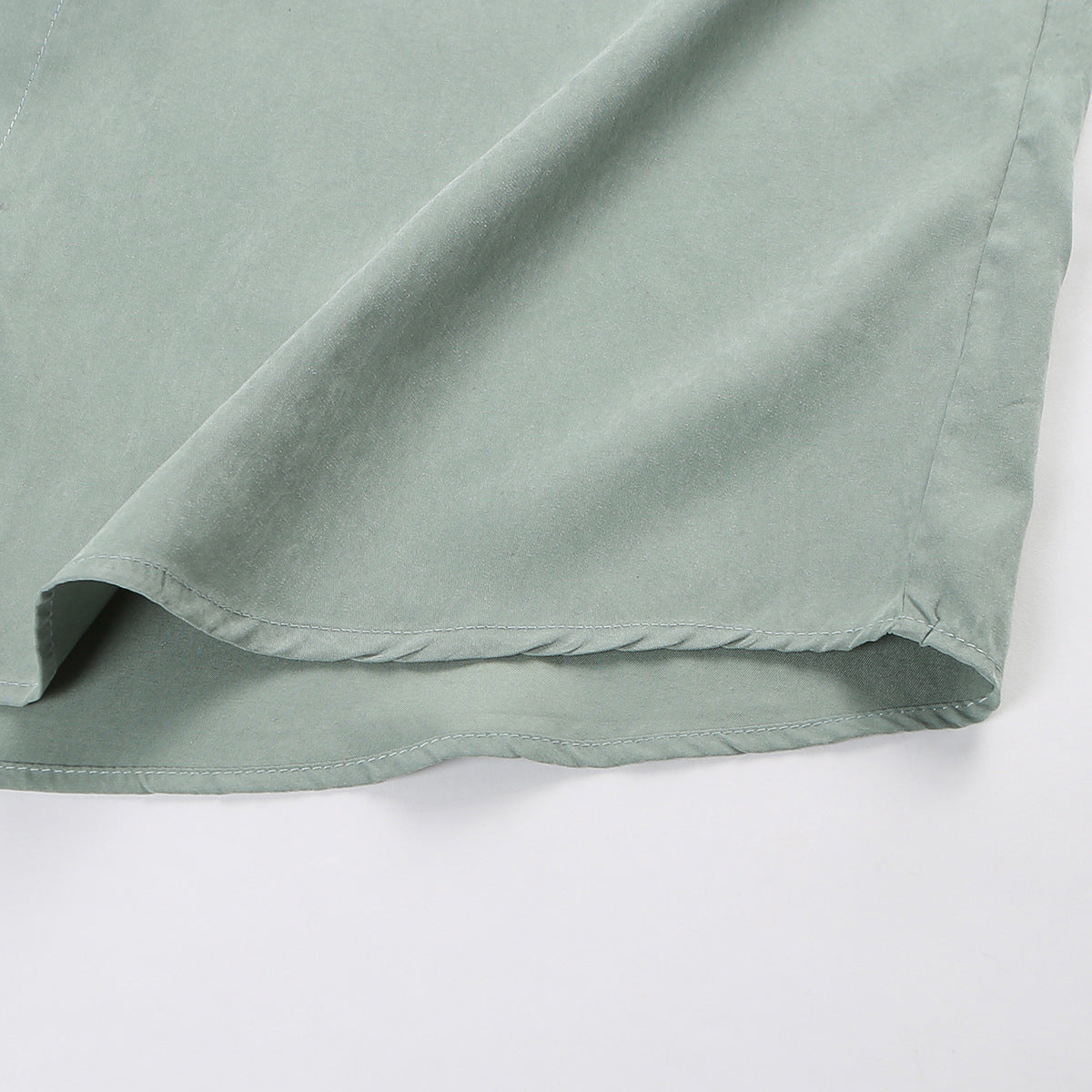 Close-up of the sage-green shirt's curved hem and double-row stitching.