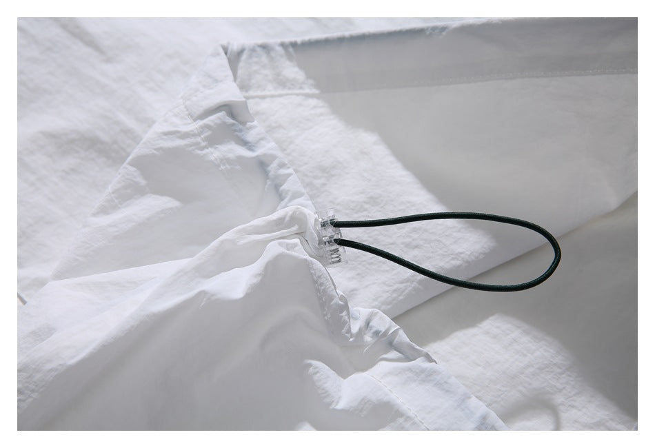 White garment close-up showing a dark green drawcord loop threaded through a clear plastic toggle.