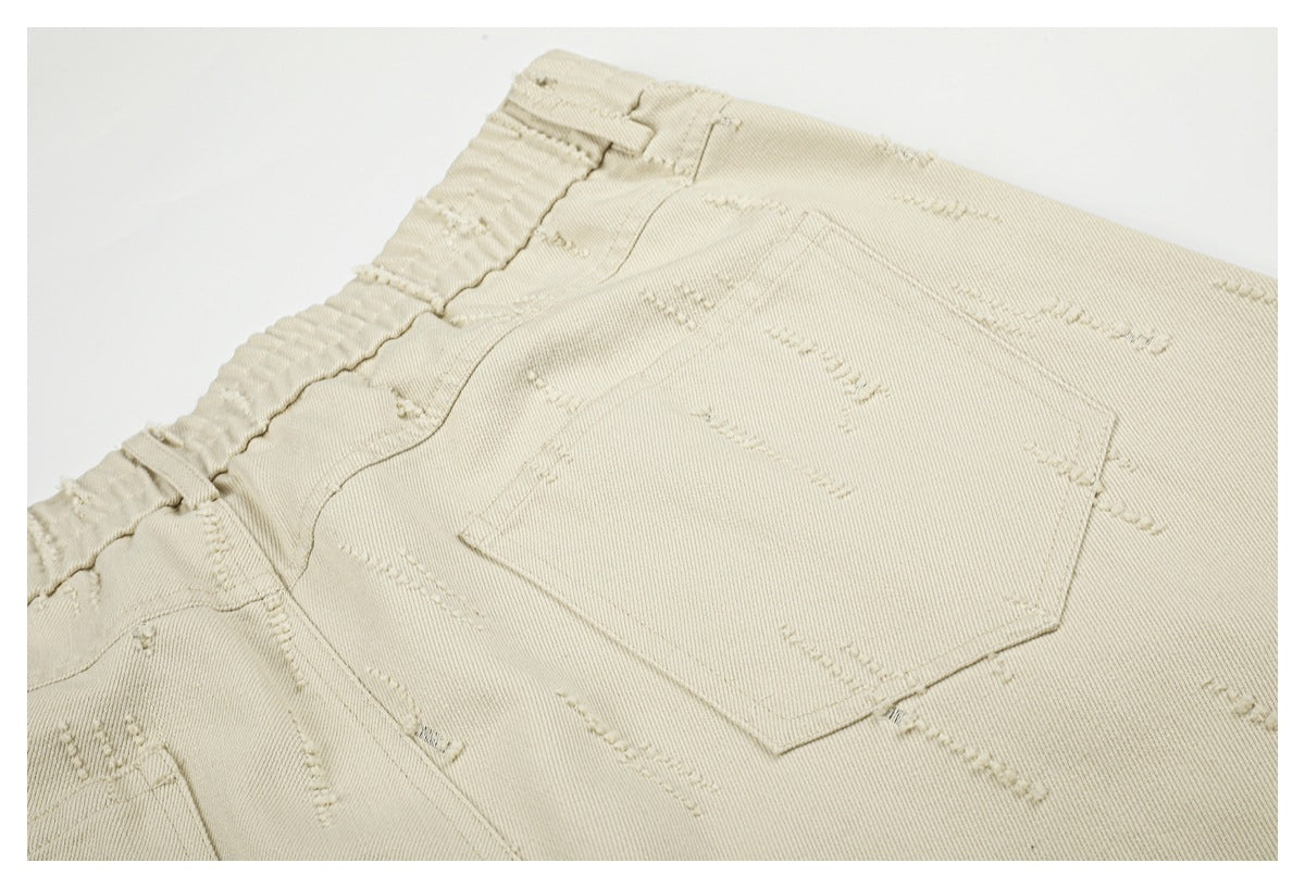 Close-up of a beige trouser back pocket and waistband, with raised decorative stitching across the fabric.