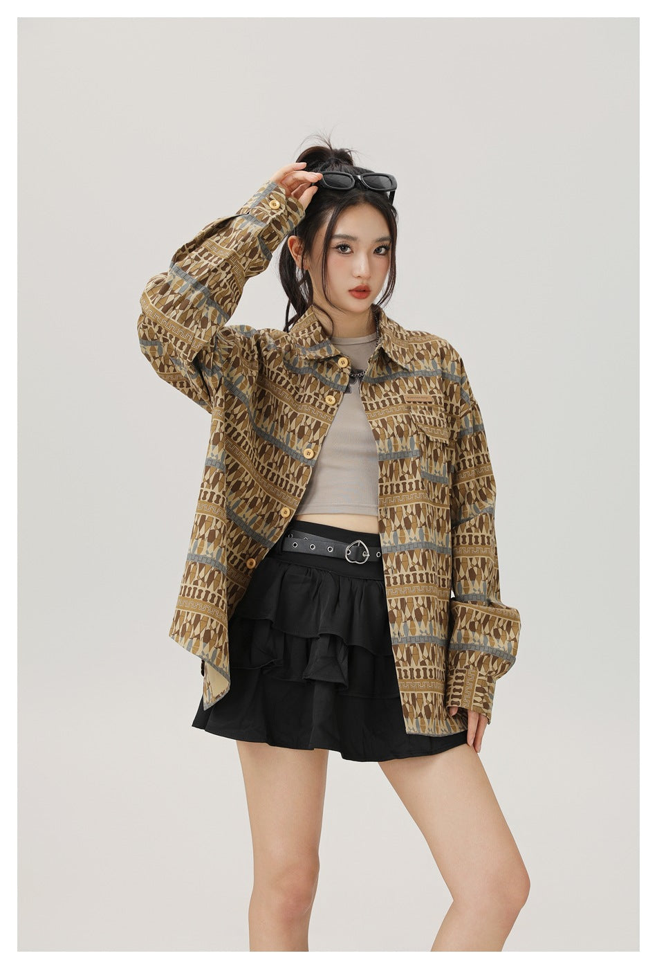 Model wearing the brown patterned shirt open over a gray cropped top and black tiered mini skirt, one arm raised