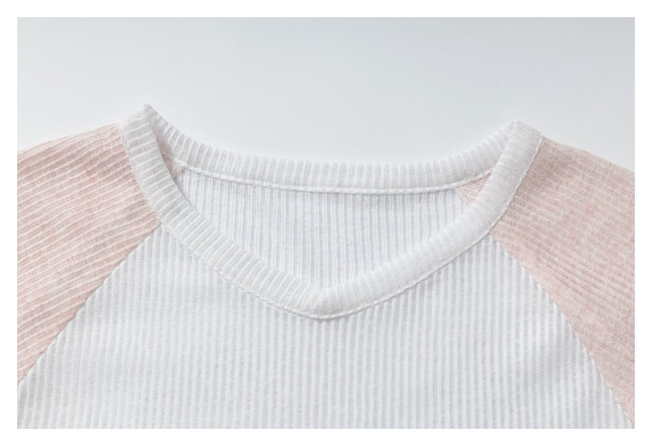 Close-up of a white ribbed V-neck and raglan shoulder seams with pale pink sleeves.