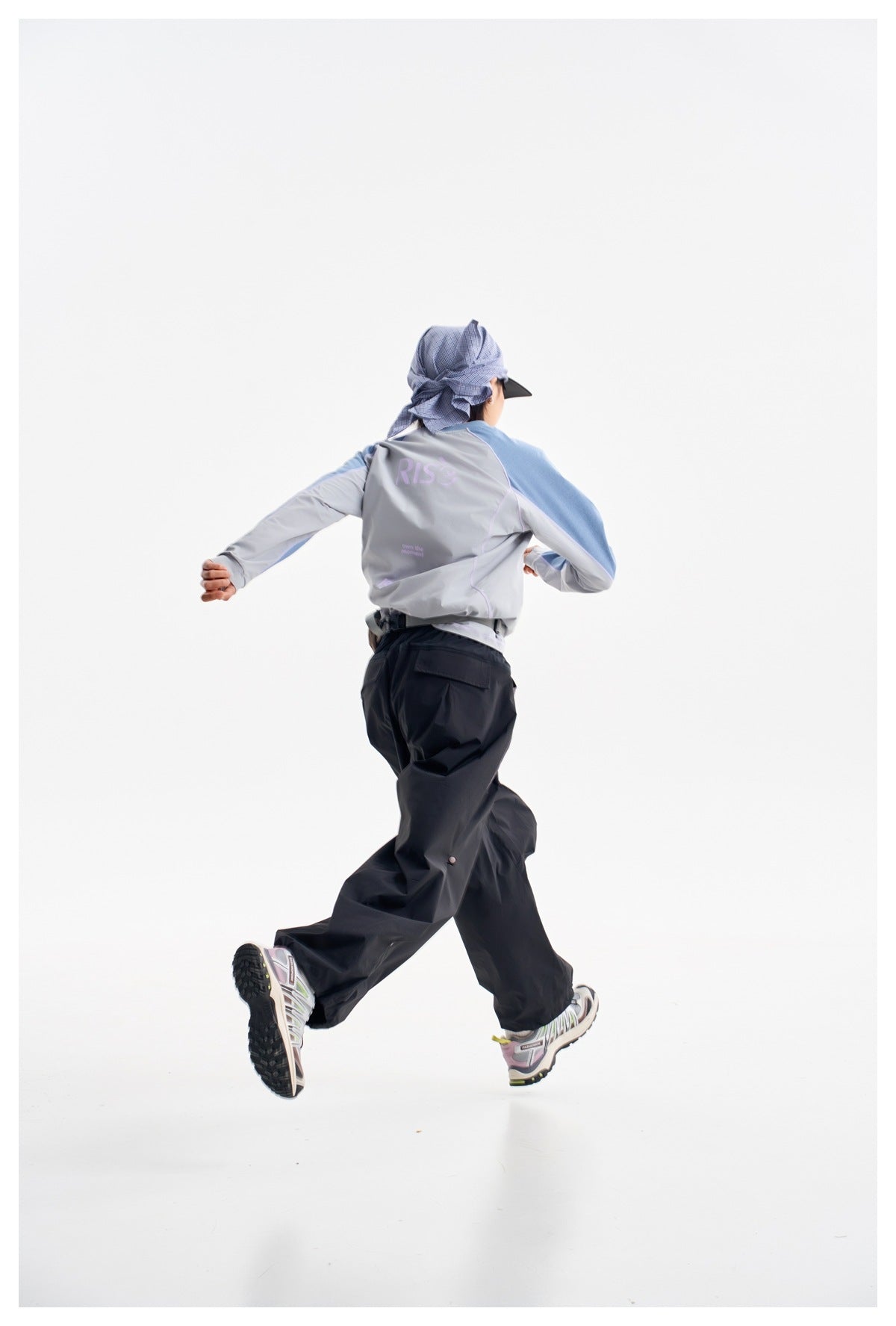 Rear view of model in a gray top with blue sleeves and dark pants; the shirt has pale lettering on the back.