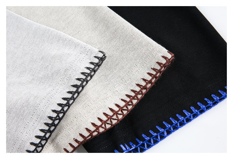 Close-up of light gray and black fabric panels with contrasting blanket stitching in black, brown, and blue.
