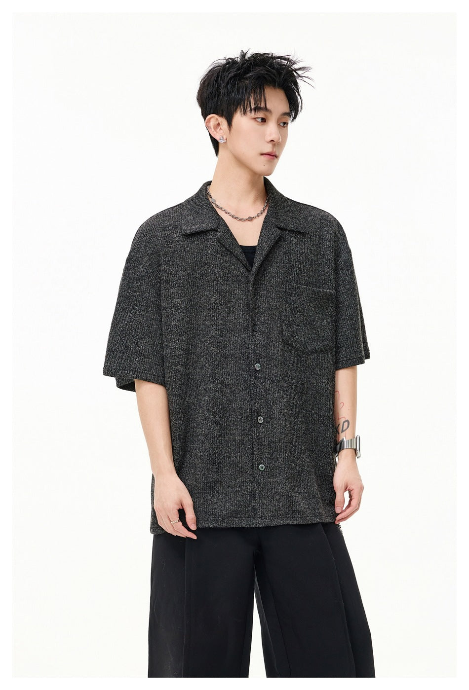 Model wearing a charcoal gray short-sleeve button-up shirt with a notched collar, chest pocket, and black trousers.