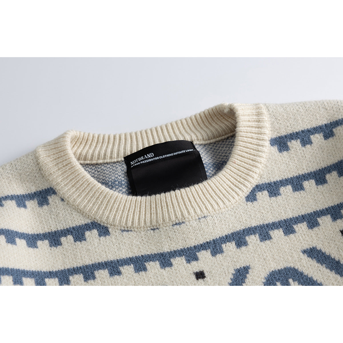Close-up of an ivory crew-neck sweater with blue geometric patterning and a black sewn-in neck label.