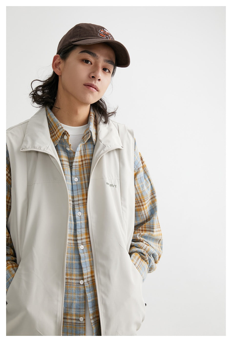 Close view of a model wearing a light gray zip-front vest over a blue and tan plaid shirt.