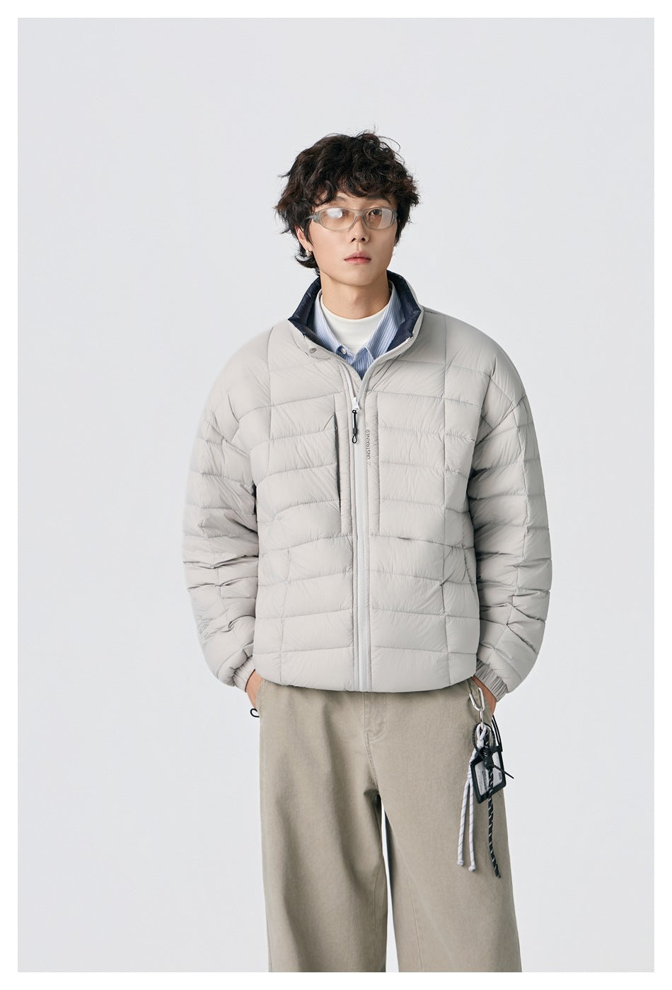 Front view of a model in a light gray quilted zip jacket with a dark inner collar and beige trousers.
