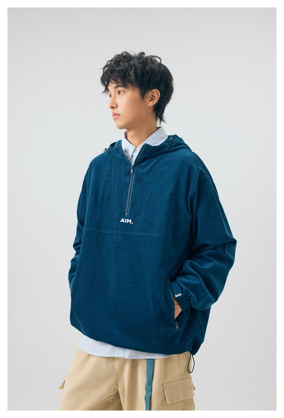 Three-quarter view of a model wearing a navy hooded pullover with a short zip and beige cargo pants.