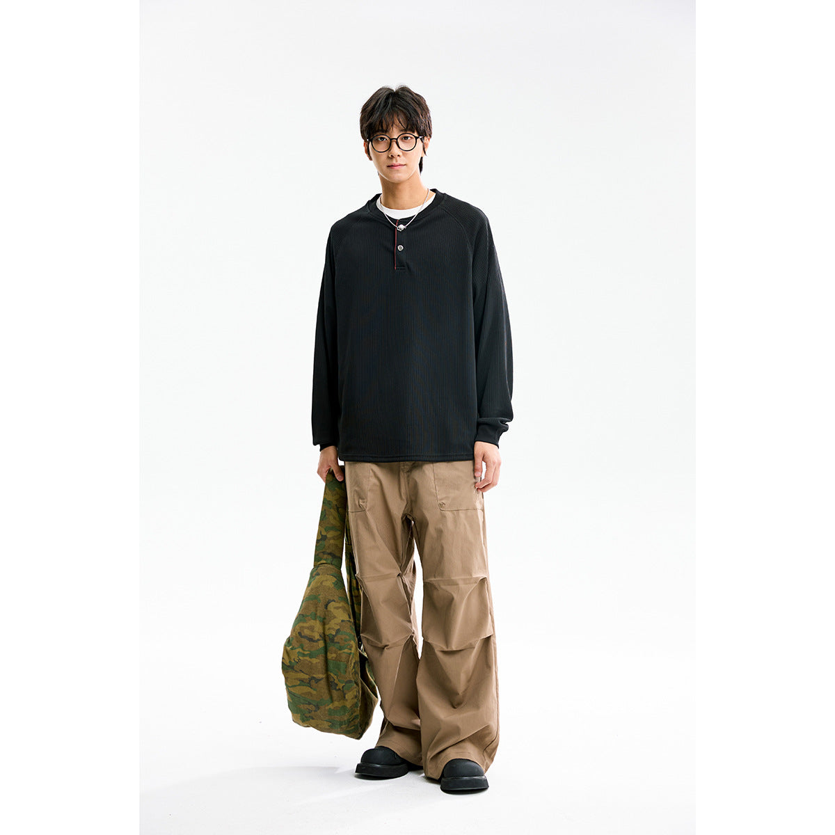 Model wearing a black long-sleeve Henley shirt with a two-button placket and loose tan cargo pants.