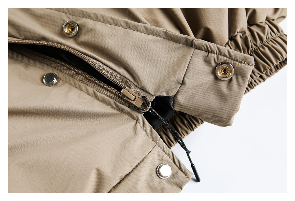 Close-up of a tan garment's zipper, snap fasteners, and gathered elastic edge.
