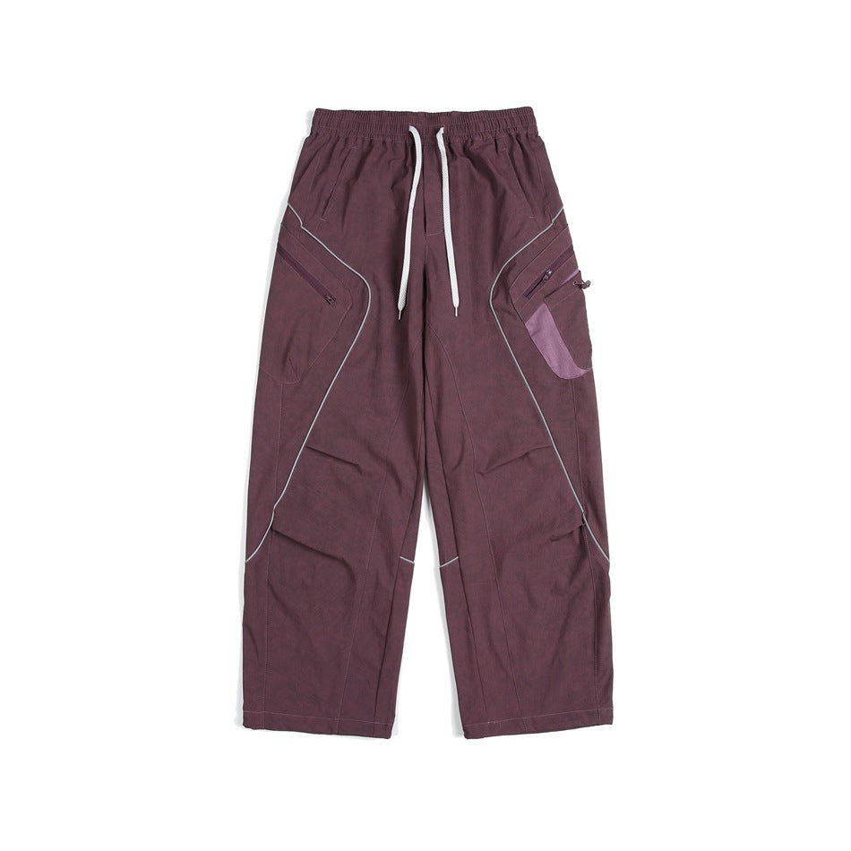 Front view of loose plum cargo pants with an elastic waist, white drawstrings, curved piping and zip pockets.