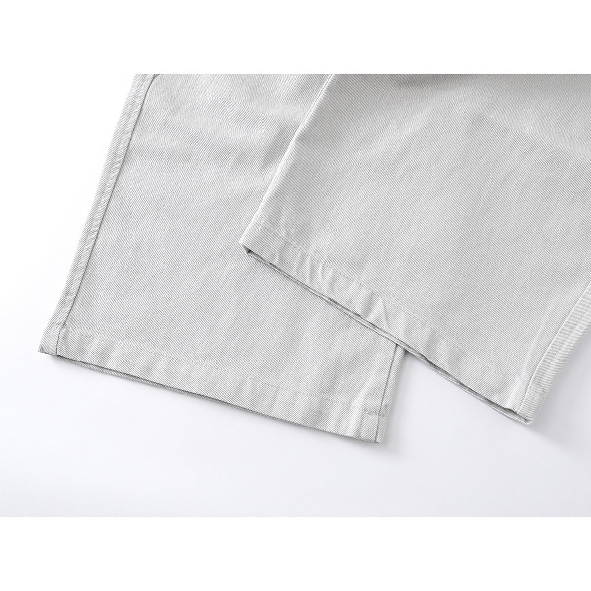 Close-up of the wide hems and stitched seams on light gray trousers.