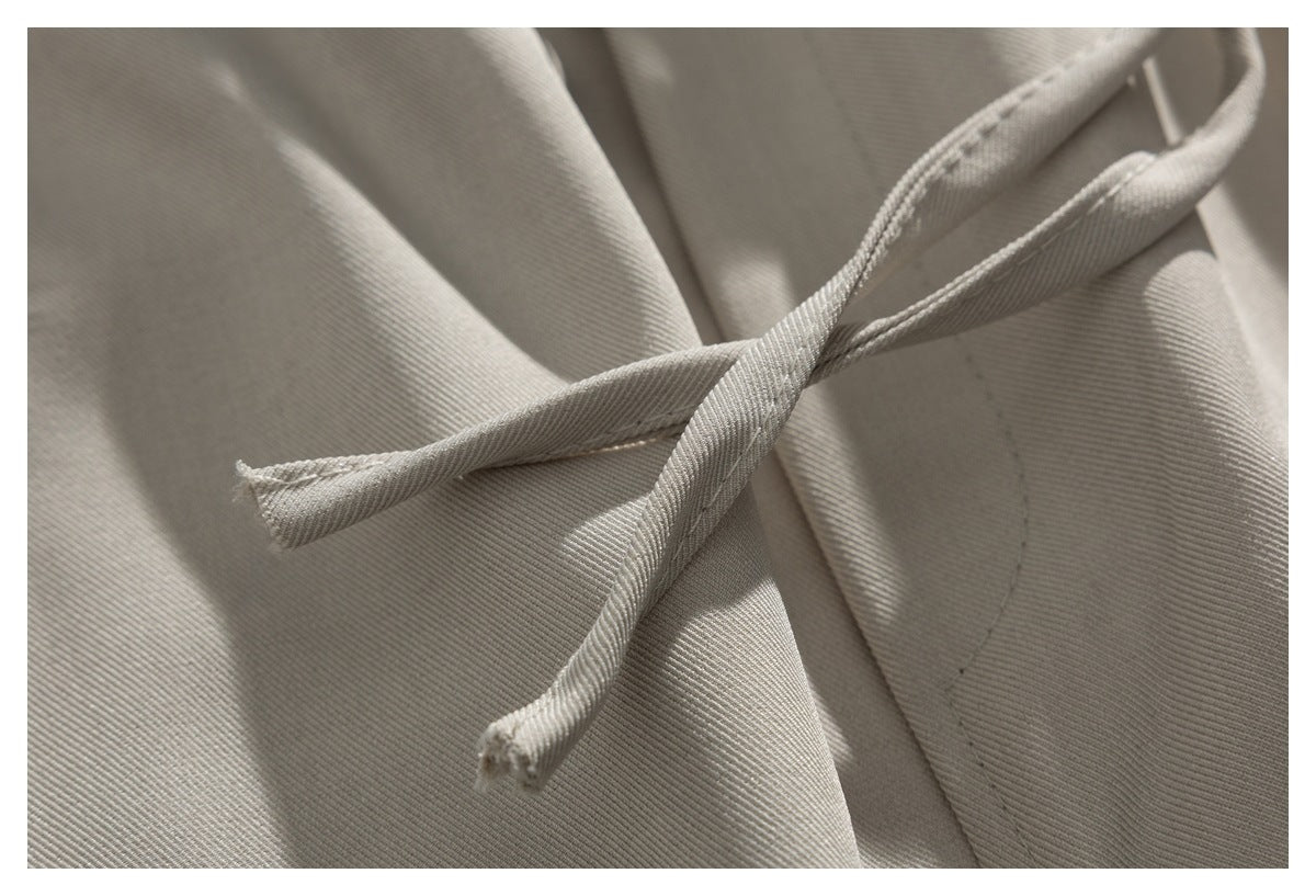 Close-up of two beige trouser drawstrings crossing over the fabric.