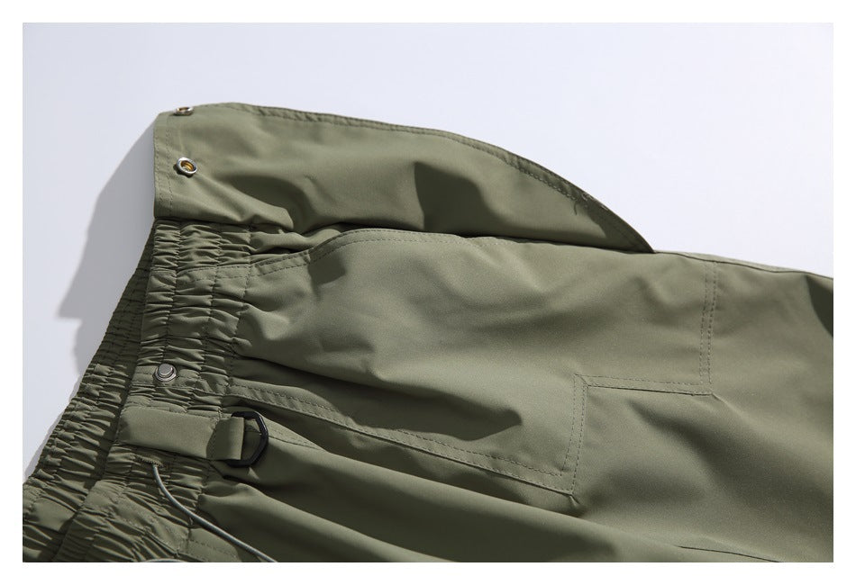 Olive-green trousers detail showing an elastic waistband, drawcord, metal eyelets and a pocket.