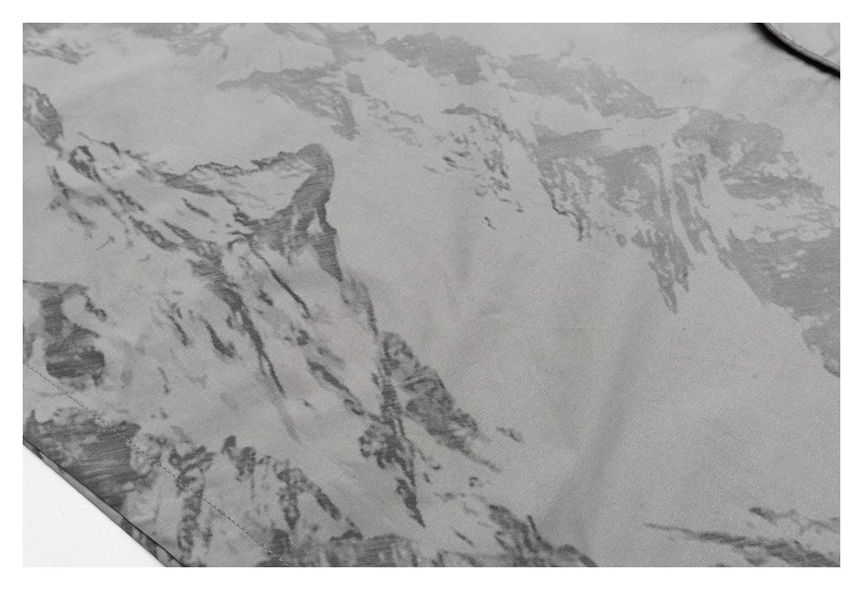 Close-up of gray fabric with an abstract, mottled camouflage-like pattern and a stitched edge.