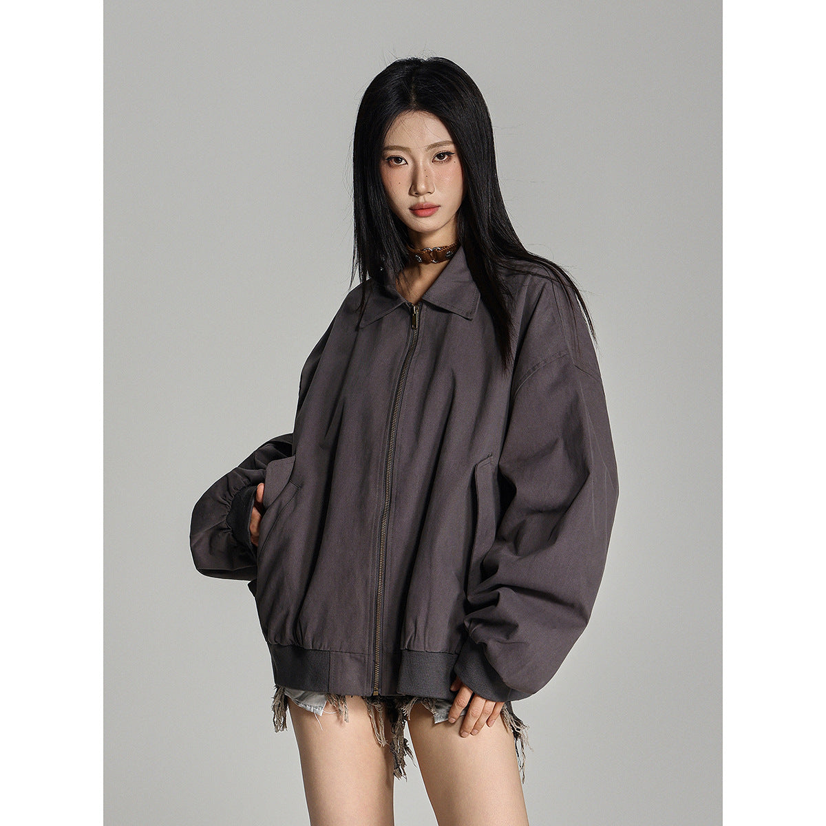 Closer view of a model wearing a charcoal-gray oversized zip jacket with a pointed collar, elastic cuffs and hem, and