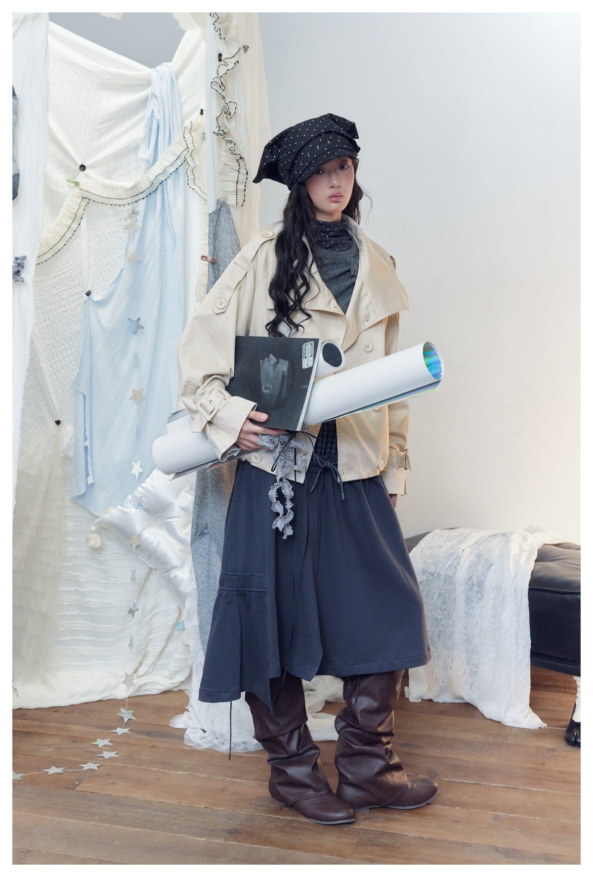 Full-length model in a cream oversized jacket, gray top, navy skirt-like bottoms, and black polka-dot headscarf.