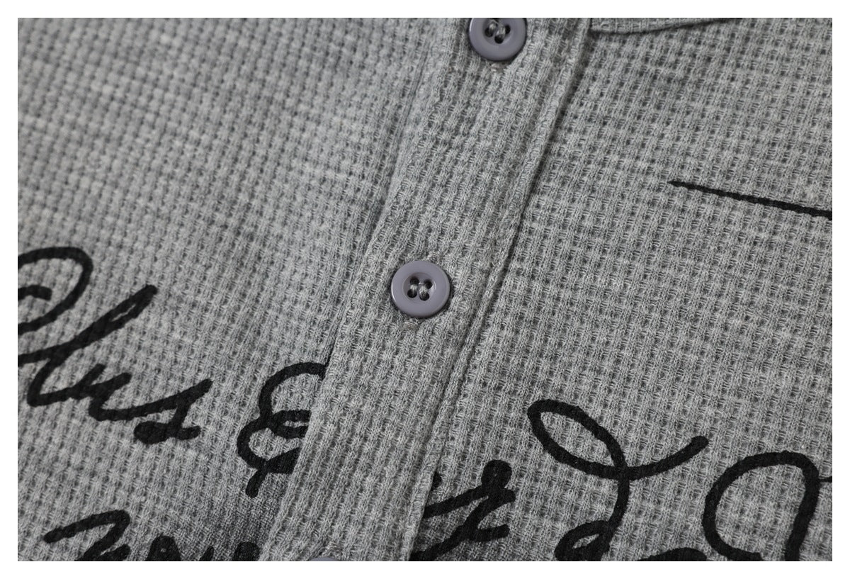 Close-up of a gray waffle-knit button-front top with black script print and a narrow seam.