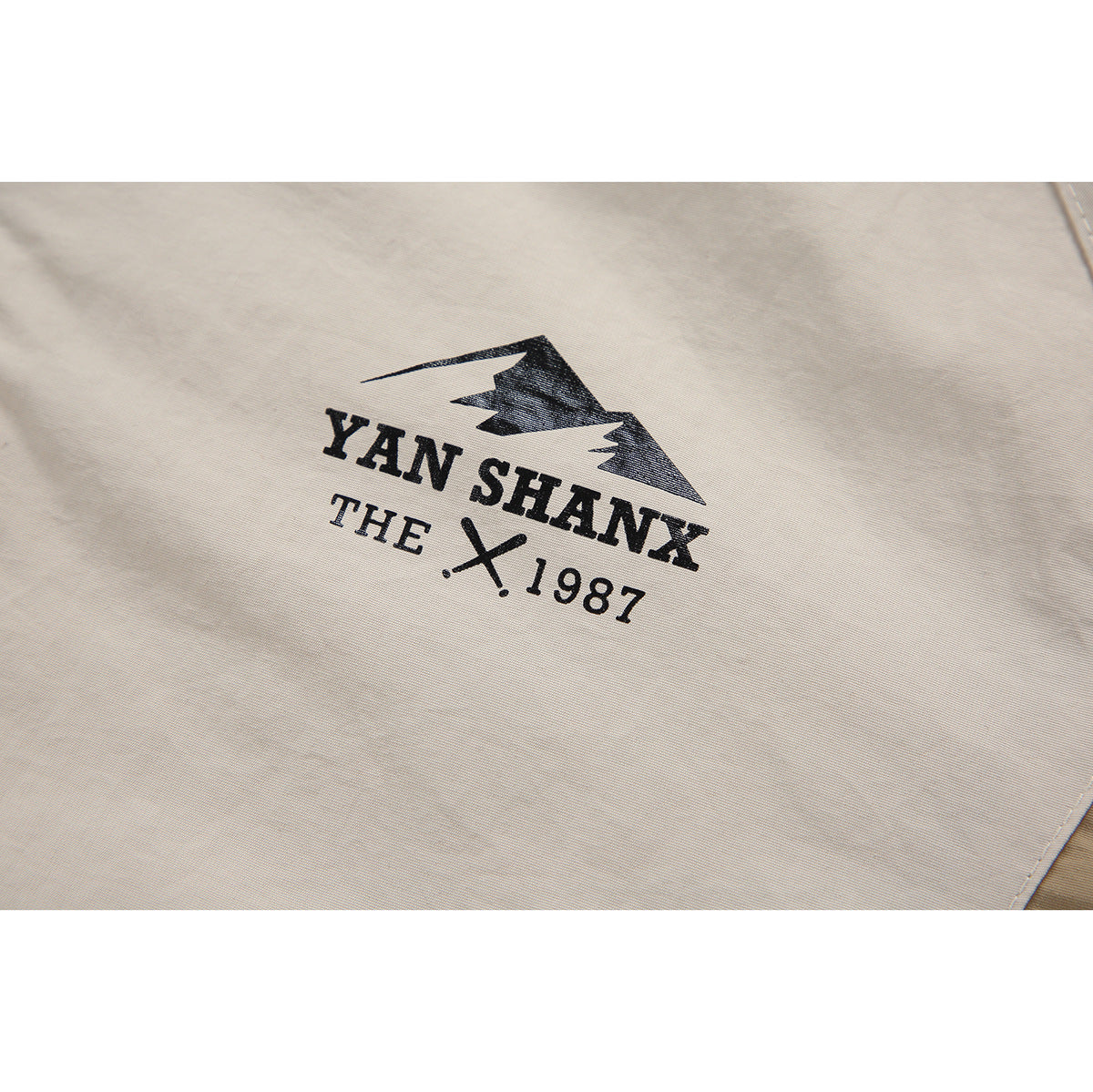 Close-up of a black mountain graphic and English lettering printed on cream jacket fabric.