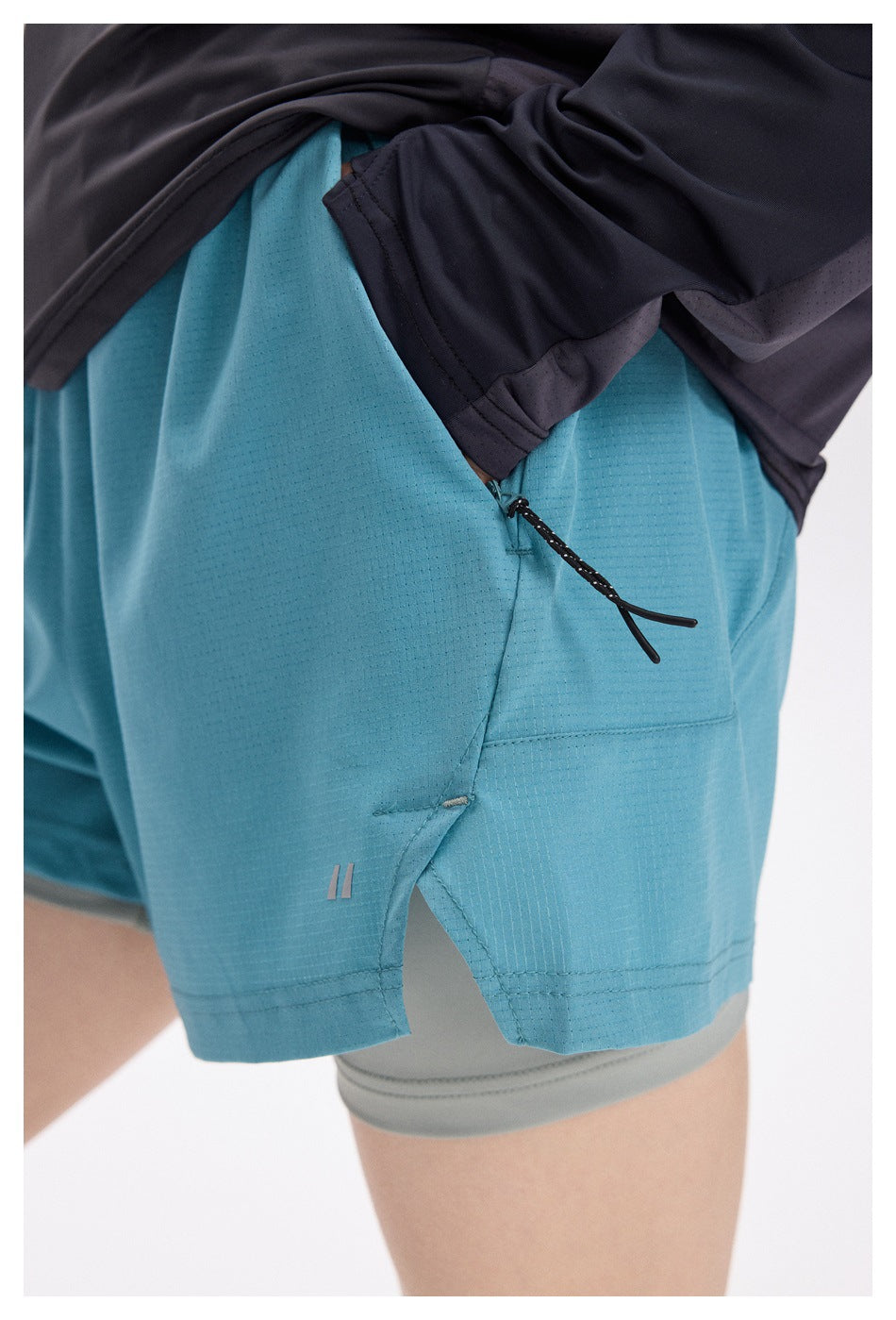 Close-up of turquoise running shorts showing a zip pocket, drawcord, stitching, and gray inner shorts.