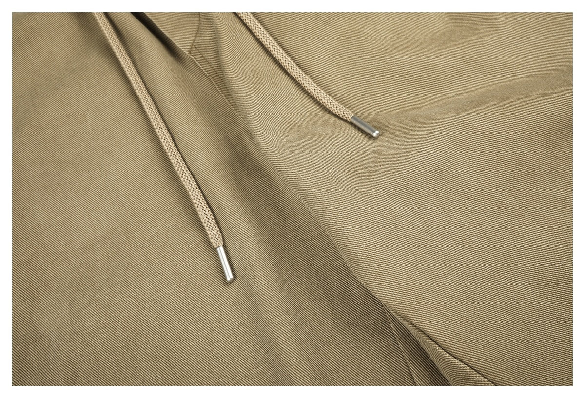 Close-up of khaki trouser fabric and two braided waist drawstrings with metal tips.